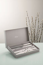 Load image into Gallery viewer, A Grey wall and a glass work top. There are willow branches in the background. The Aynsley Charbagh Pastry Set sits in its grey gift box. Stainless Steel with White Fine porcelain handles. A delicate persian and indian inspired motif on each handle. The set contains 1 cake slice, 1 serrated blade cake knife and 4 pastry forks.