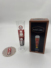 Load image into Gallery viewer, Tall slim Pilsner style beer glass wih red and black beer pump in the style of an american fuel pump. Matching checkered flag beer mat is to its left and gift box to its right.
