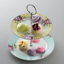 Load image into Gallery viewer, A grey background. This is an image of the Aynsley Archive Rose 2 Tier cake stand holding petit fours and lilac, lemon and pink coloured macarons. The tops plate has a yellow border. The bottom plate has a blue border. Both plates have pink rose and green leaf motifs. The pieces holding the cake stand together are silver in colour.
