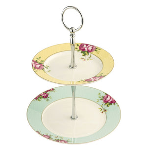 White background. Aynsley Archive Rose 2 tier cake stand. The Plate on the bottom has a blue board with pink roses and green leaves. The plate on the top has a yellow border with pink roses and green leaves. The Cake stand pieces holding it together are silver in colour.