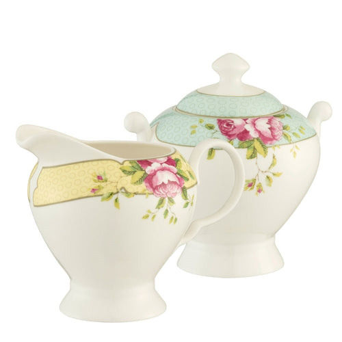 White Background. Aynsley Archive Rose Cream Jug and Covered Sugar Bowl. The Cream jug is white fine china with a yellow band around the rim. Decorated with delicate circles, pink roses and green leaves. The sugar bowl is white fine china with a blue band around with lid with delicate circles on the band. And a blue band around the rim of the bowl. There are pink roses and green leaves motifs on either side of the bowl, on the blue band. The bowl has 2 handles.
