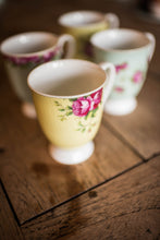 Load image into Gallery viewer, A close up of a Yellow footed mug on a wooden dining table and 3 other mugs from the set blurred into the background. This is a close up of the pink rose motif.
