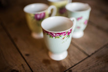 Load image into Gallery viewer, A close up of a blue footed mug on a wooden dining table and 3 other mugs from the set blurred into the background. This is a close up of the pink rose motif.
