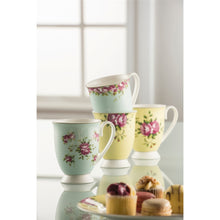 Load image into Gallery viewer, 4 Aynsley Archive Rose footed mugs on a reflective worktop, in from of a window. There are 2 blue mugs and 2 yellow mugs. All with pink rose, green leaves and a delicate circles all over the motif. There is an Archive Rose yellow tea plate in the foreground with petit fours.

