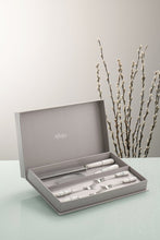 Load image into Gallery viewer, A Grey wall and a glass work top. There are willow branches in the background. The Aynsley Charbagh Pastry Set sits in its grey gift box. Stainless Steel with White Fine porcelain handles. A delicate persian and indian inspired motif on each handle. The set contains 1 cake slice, 1 serrated blade cake knife and 4 pastry forks.
