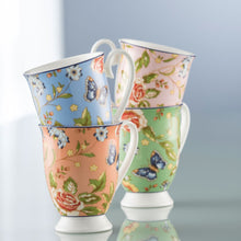 Load image into Gallery viewer, A Blue Grey Background. Aynsley Cottage Garden Set of 4 Footed Mugs. Fine White Porcelain mugs. 1 Blue, 1 Pink, 1 Coral and 1 Green. They all have the rose, daisy, leaves and blue butterfly pattern all over these background colours. Sitting on a reflective surface.
