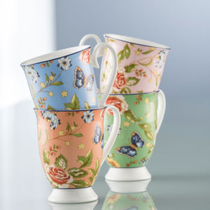 A Blue Grey Background. Aynsley Cottage Garden Set of 4 Footed Mugs. Fine White Porcelain mugs. 1 Blue, 1 Pink, 1 Coral and 1 Green. They all have the rose, daisy, leaves and blue butterfly pattern all over these background colours. Sitting on a reflective surface.