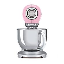 Load image into Gallery viewer, White Background. Smeg 50s Retro Stand Mixer. The top of the mixer is Pink, the base is silver. There are the letters S, M, E and G embossed in chrome on either side of the machine. It has a Stainless Steel 4.8L bowl and beaters. The speed control is a chrome level on the top of the machine. The top lifts up by pressing in a button at the back of the motor case.

