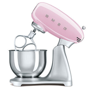 White Background. Smeg 50s Retro Stand Mixer. The top of the mixer is Pink, the base is silver. There are the letters S, M, E and G embossed in chrome on either side of the machine. It has a Stainless Steel 4.8L bowl and beaters. The speed control is a chrome level on the top of the machine. The top lifts up by pressing in a button at the back of the motor case.
