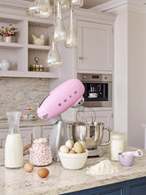 Load image into Gallery viewer, Lifestyle Image. Set in a Cream kitchen surrounded by baking ingredients. Smeg 50s Retro Stand Mixer. The top of the mixer is Pink, the base is silver. There are the letters S, M, E and G embossed in chrome on either side of the machine. It has a Stainless Steel 4.8L bowl and beaters. The speed control is a chrome level on the top of the machine. The top lifts up by pressing in a button at the back of the motor case.
