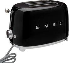 Load image into Gallery viewer, White Background. Black Smeg 50&#39;s Style Retro 2 Slice Toaster with silver embossed letters S M E and G across the front. A silver press down lever, turning temperature knob, defrost, reheat and stop buttons. The toaster is chrome at the top and bottom.

