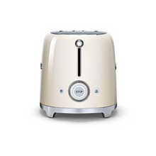 Load image into Gallery viewer, A side view. White Background. Cream Smeg Retro 50&#39;s style 2 slicer toaster. It has a cream body, Chrome top and base with chrome embossed letters S M E and G across the front. The push down lever, browning knob, defrost, reheat and stop buttons are all chrome.
