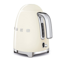 Load image into Gallery viewer, Rear side view. White Background. Smeg 50s Retro 1.7L Kettle. The body of the kettle is Cream. There are chrome letters S, M, E and G embossed on each side. The lid is push button release. The spout, Handle, on/off lever and base are chrome. There is a water level window in line with the handle.
