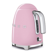 Load image into Gallery viewer, Rear Side View. White Background. Smeg 50s Retro 1.7L Kettle. The body of the kettle is Pink. There are chrome letters S, M, E and G embossed on each side. The lid is push button release. The spout, Handle, on/off lever and base are chrome. There is a water level window in line with the handle.
