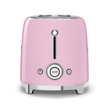 Load image into Gallery viewer, Side view. White Background. Smeg Pink 50s Retro 2 Slice Toaster. The body of the toaster is pink with chrome letters S, M, E and G embossed on both sides. The top and base are chrome. The push down lever, defrost, reheat, stop buttons and browning knob are all chrome.
